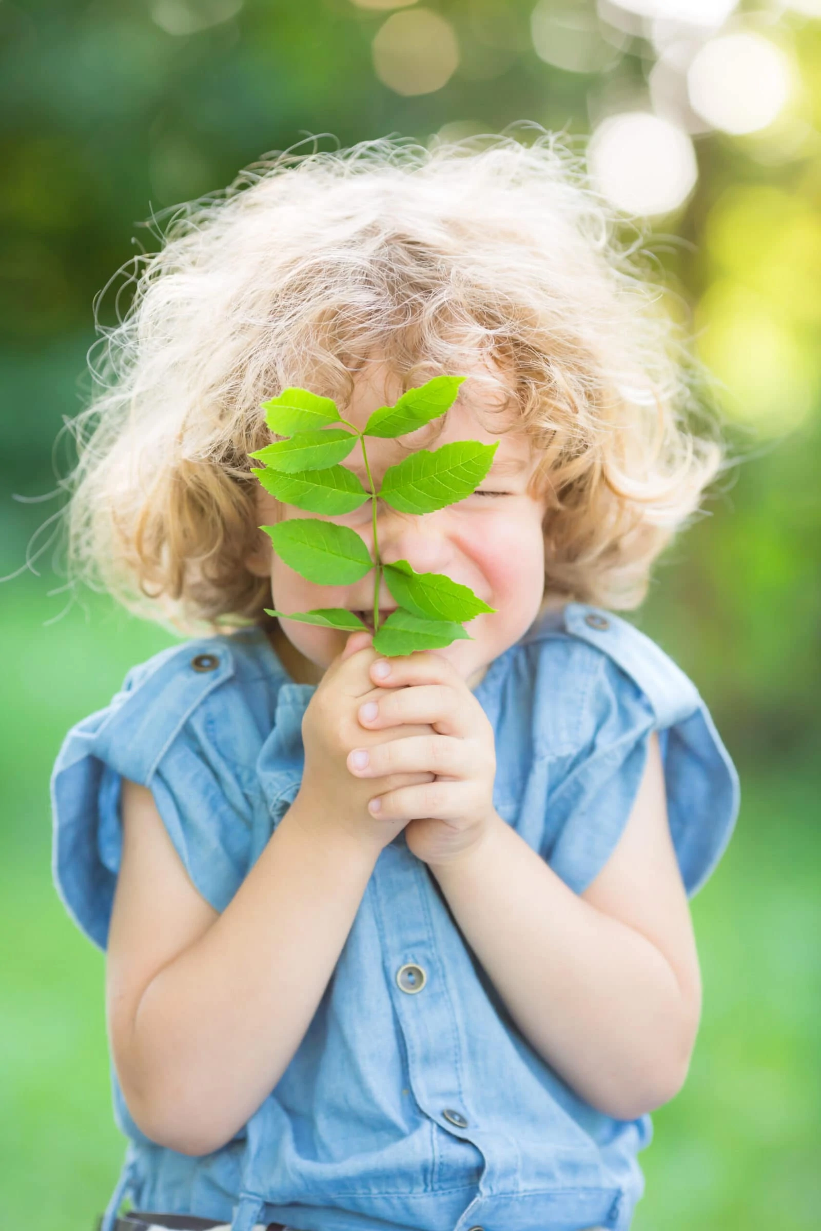 Child holds green plant in front of face